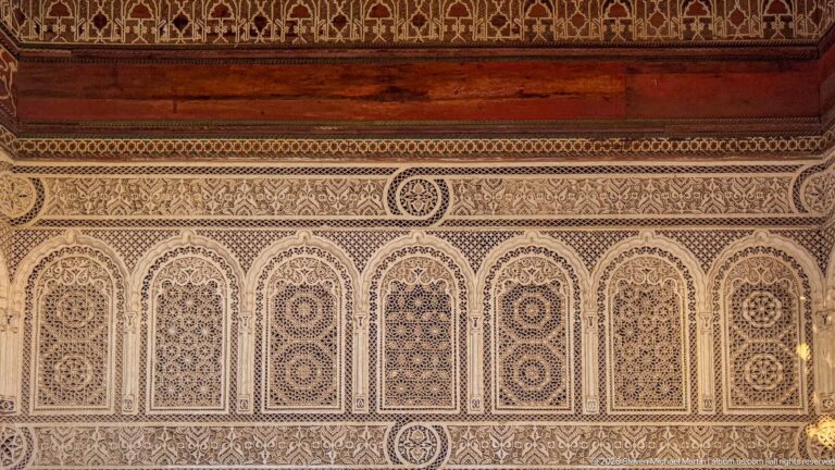 Seven carved Bahia Palace stucco arches with alternating rosette and lattice designs beneath a decorative frieze.