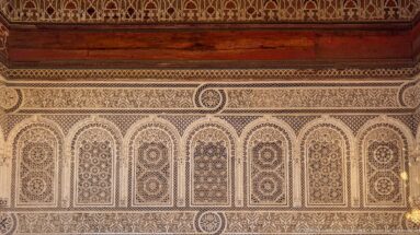 Seven carved Bahia Palace stucco arches with alternating rosette and lattice designs beneath a decorative frieze.