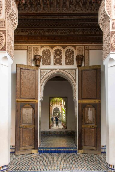 Wide symmetrical Bahia Palace interior with open wooden doors, carved arch, painted ceiling and geometric tiled floor.