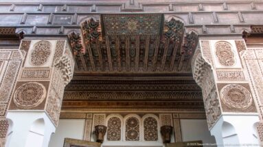 Upward view of a painted wooden ceiling between carved plaster piers with dense geometric and vegetal ornament.