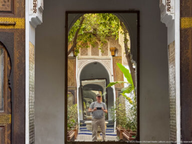 Visitor framed by successive decorated doorways leading through a tiled, planted courtyard at Bahia Palace.