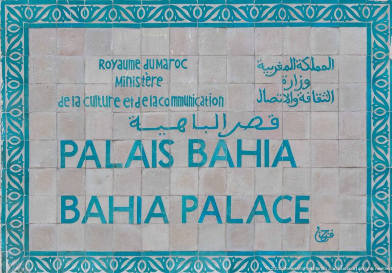 Official Bahia Palace sign with Arabic, French and English lettering inside a turquoise ornamental border.