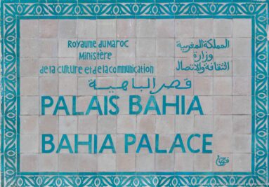 Official Bahia Palace sign with Arabic, French and English lettering inside a turquoise ornamental border.