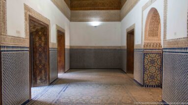 Bahia Palace room with geometric zellij wall tiles, wooden doors, carved arched opening and painted ceiling.