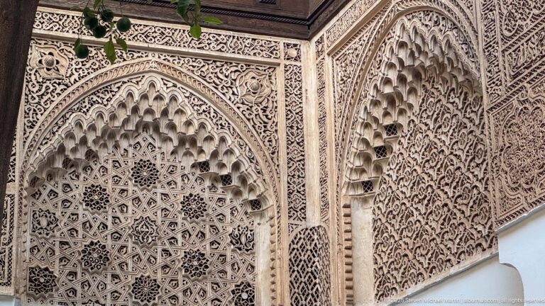 Close view of deeply carved Bahia Palace plaster arches with honeycomb niches, geometric stars and dense vegetal relief.