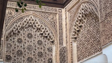 Close view of deeply carved Bahia Palace plaster arches with honeycomb niches, geometric stars and dense vegetal relief.