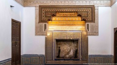 Decorated Bahia Palace fireplace with dark firebox, geometric zellij, carved surround and projecting ornamental hood.