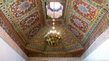 Ornate polychrome coffered ceiling at Bahia Palace with floral-geometric panels, central raised opening and hanging chandelier.