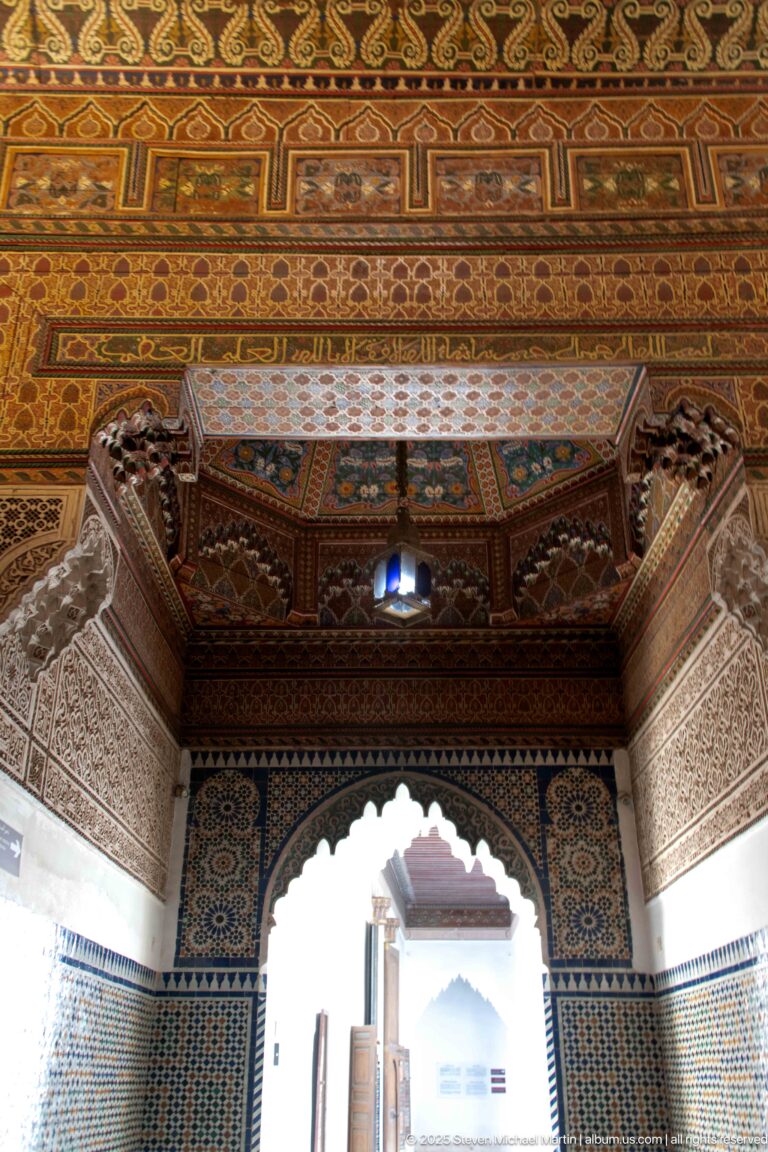 Scalloped Bahia Palace arch surrounded by zellij and carved plaster beneath an elaborately painted timber ceiling.