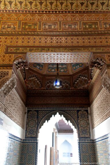 Scalloped Bahia Palace arch surrounded by zellij and carved plaster beneath an elaborately painted timber ceiling.