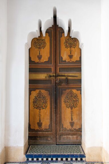Painted double doors with stylized floral-tree motifs set in a scalloped white niche at Bahia Palace.
