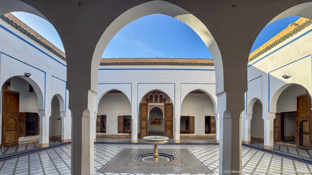 Bahia Palace courtyard and fountain framed by large foreground arches beneath a blue sky.