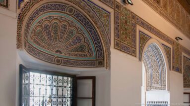 Painted fan-shaped arch panels with blue-green geometric and vegetal ornament above Bahia Palace wall openings.