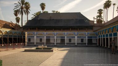 Bahia Palace courtyard with central fountain, blue-white arcades and a large dark protective cover over one building wing.
