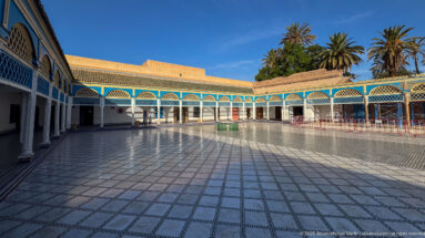 Expansive Bahia Palace courtyard with gridded tiled pavement, blue-white galleries, small central basin and palms.