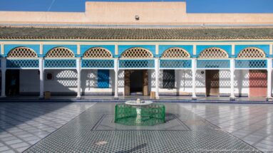 Green-tiled courtyard basin aligned with a blue-and-white arcade and wooden doorways at Bahia Palace.
