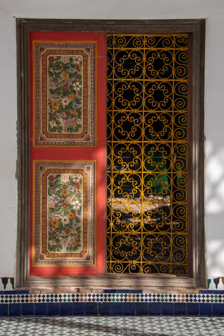 Floral-painted wooden shutters beside a black scrolling metal grille at Bahia Palace.