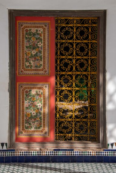 Floral-painted wooden shutters beside a black scrolling metal grille at Bahia Palace.