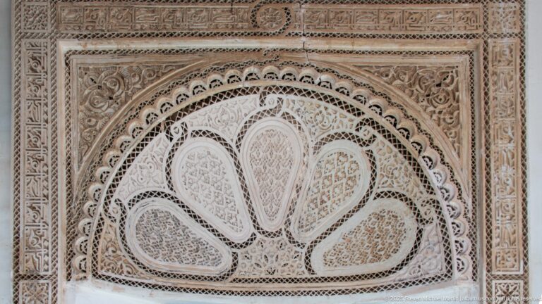 Fan-shaped carved plaster lunette with teardrop compartments, vegetal scrolls and geometric borders at Bahia Palace.