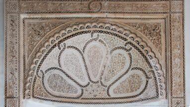 Fan-shaped carved plaster lunette with teardrop compartments, vegetal scrolls and geometric borders at Bahia Palace.