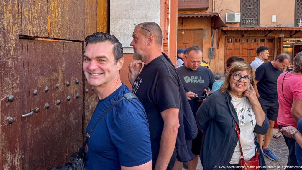 Visitors gathered beside the large studded wooden entrance doors of Bahia Palace in Marrakech.