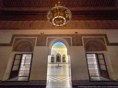 Bahia Palace salon with painted ceiling, hanging chandelier, decorated window lunettes and an arched doorway to the courtyard.