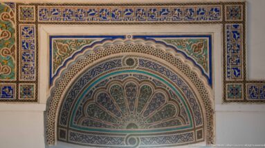Blue-green painted fan-shaped lunette with scalloped arch and dense geometric-floral ornament at Bahia Palace.