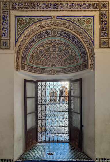 Painted blue-green lunette above a barred window with open wooden shutters at Bahia Palace.