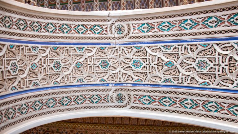 Close Bahia Palace carved plaster with lattice-like vegetal relief, geometric bands and turquoise accents above an arch.