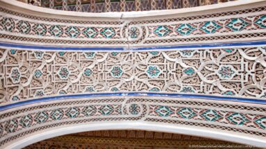Close Bahia Palace carved plaster with lattice-like vegetal relief, geometric bands and turquoise accents above an arch.