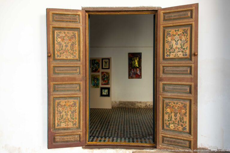 Open floral-painted double doors at Bahia Palace framing a tiled room with framed works on white walls.