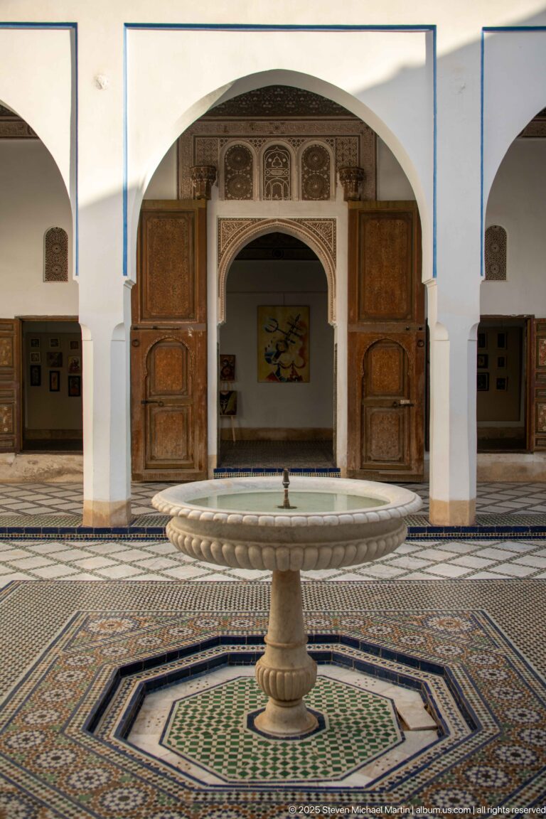 Bahia Palace pedestal fountain centered before an arched doorway, open wooden doors and geometric zellij paving.