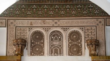 Carved Bahia Palace stucco panel with three arches, circular rosette medallions, projecting capitals and painted floral band above.