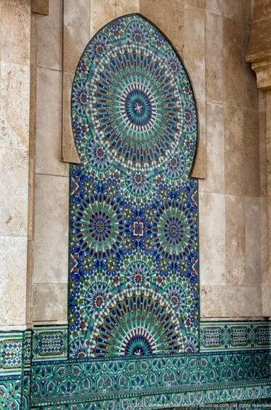 Blue-green zellij wall niche with concentric rosettes, radial geometric patterns and a tiled band along the base.