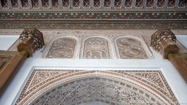 Carved Bahia Palace arch with three stucco panels, projecting brackets and a painted timber frieze above.