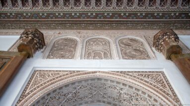 Carved Bahia Palace arch with three stucco panels, projecting brackets and a painted timber frieze above.