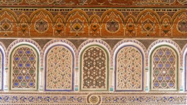 Five decorated arched Bahia Palace wall panels beneath a warm painted frieze with repeating pointed-arch motifs.
