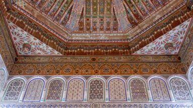 Polychrome Bahia Palace interior with painted timber ceiling and a continuous row of varied arched decorative wall panels.
