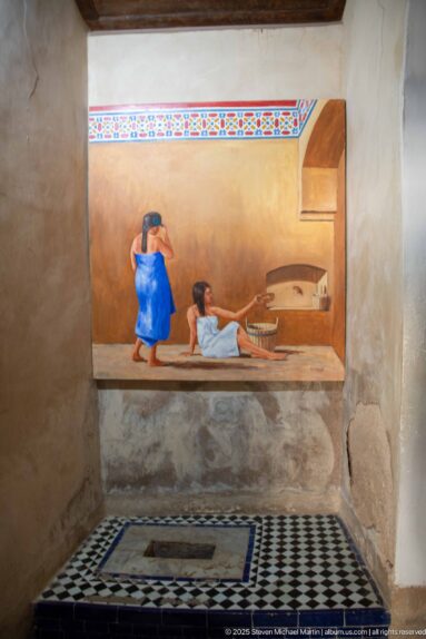 Painted hammam scene with two figures above black-and-white geometric floor tiles and a rectangular floor opening.