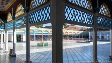 Bahia Palace large courtyard seen from a shaded gallery with dark lattice panels and slender columns.