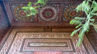 Polychrome Bahia Palace wooden ceiling corner with circular rosettes, floral patterns, framed central panel and green foliage.