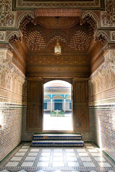 Decorated Bahia Palace passage with zellij, carved plaster and painted ceiling opening onto the bright Grande Cour.