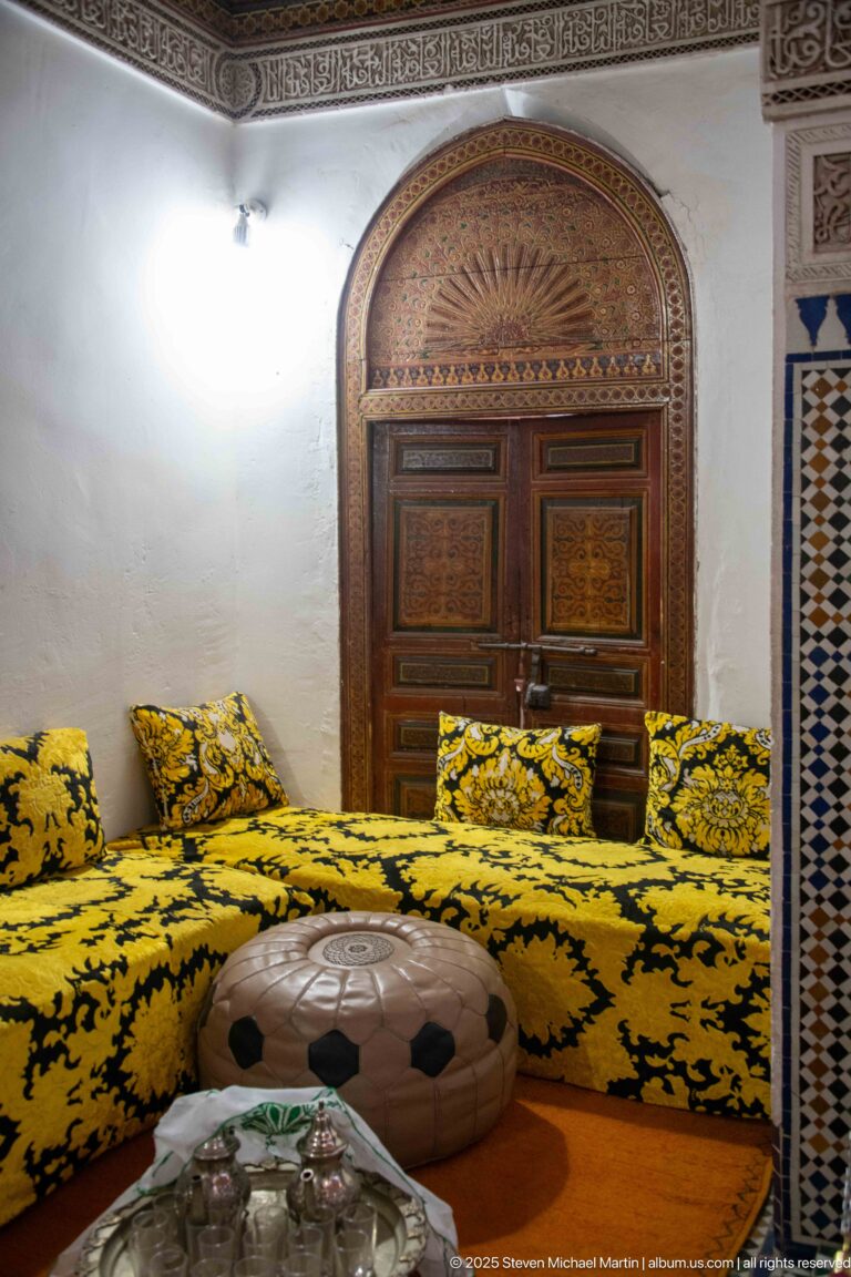 Bahia Palace riad room with yellow-and-black low seating, painted arched wooden door, round table and tea service.