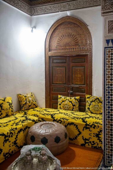 Bahia Palace riad room with yellow-and-black low seating, painted arched wooden door, round table and tea service.