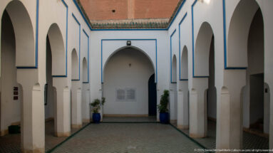 Small Bahia Palace courtyard with white pointed arches, blue trim, tiled paving and potted plants.