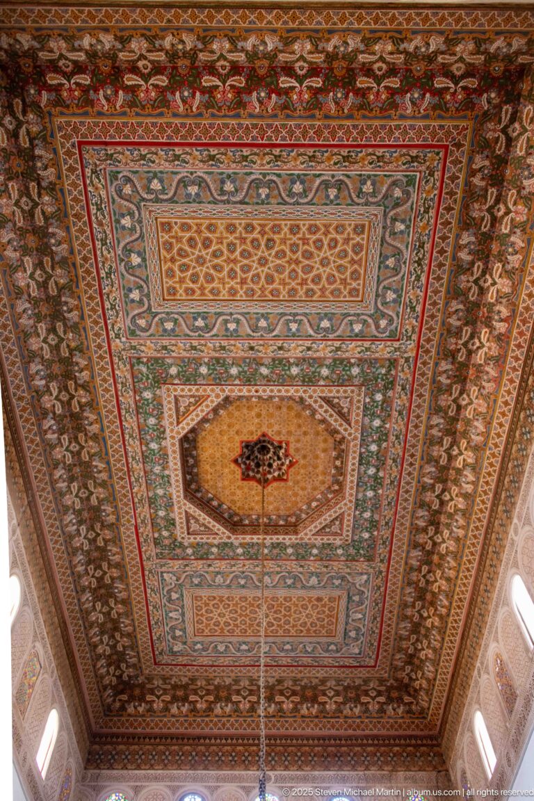 Large polychrome timber ceiling in Bahia Palace’s Grand Riad with layered rectangular fields and dense floral-geometric borders.