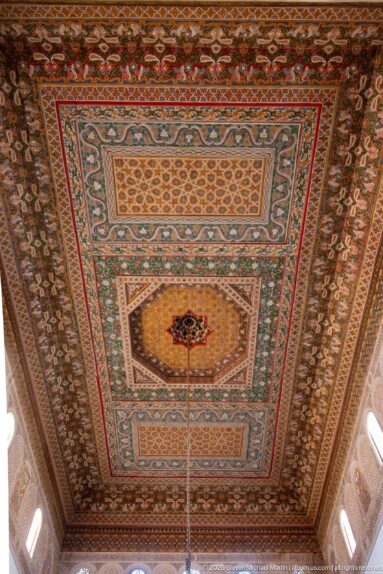 Large polychrome timber ceiling in Bahia Palace’s Grand Riad with layered rectangular fields and dense floral-geometric borders.