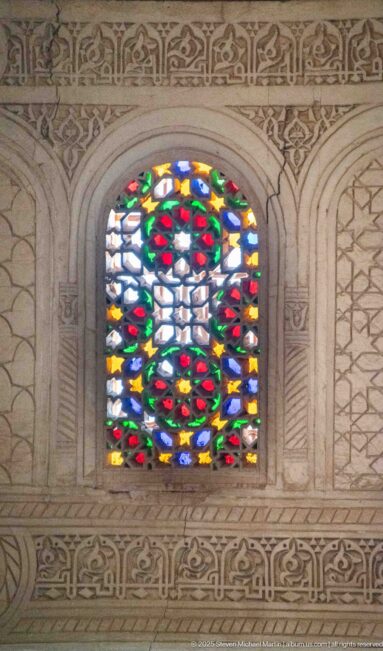 Small multicolored stained-glass window set in a carved pale plaster surround at Bahia Palace.
