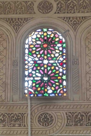 Arched Bahia Palace stained-glass window with green, red, pink, blue and yellow floral-geometric pattern.