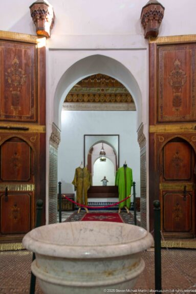Large pale stone basin aligned with successive arches, wooden cupboards and a hanging lamp inside Bahia Palace.